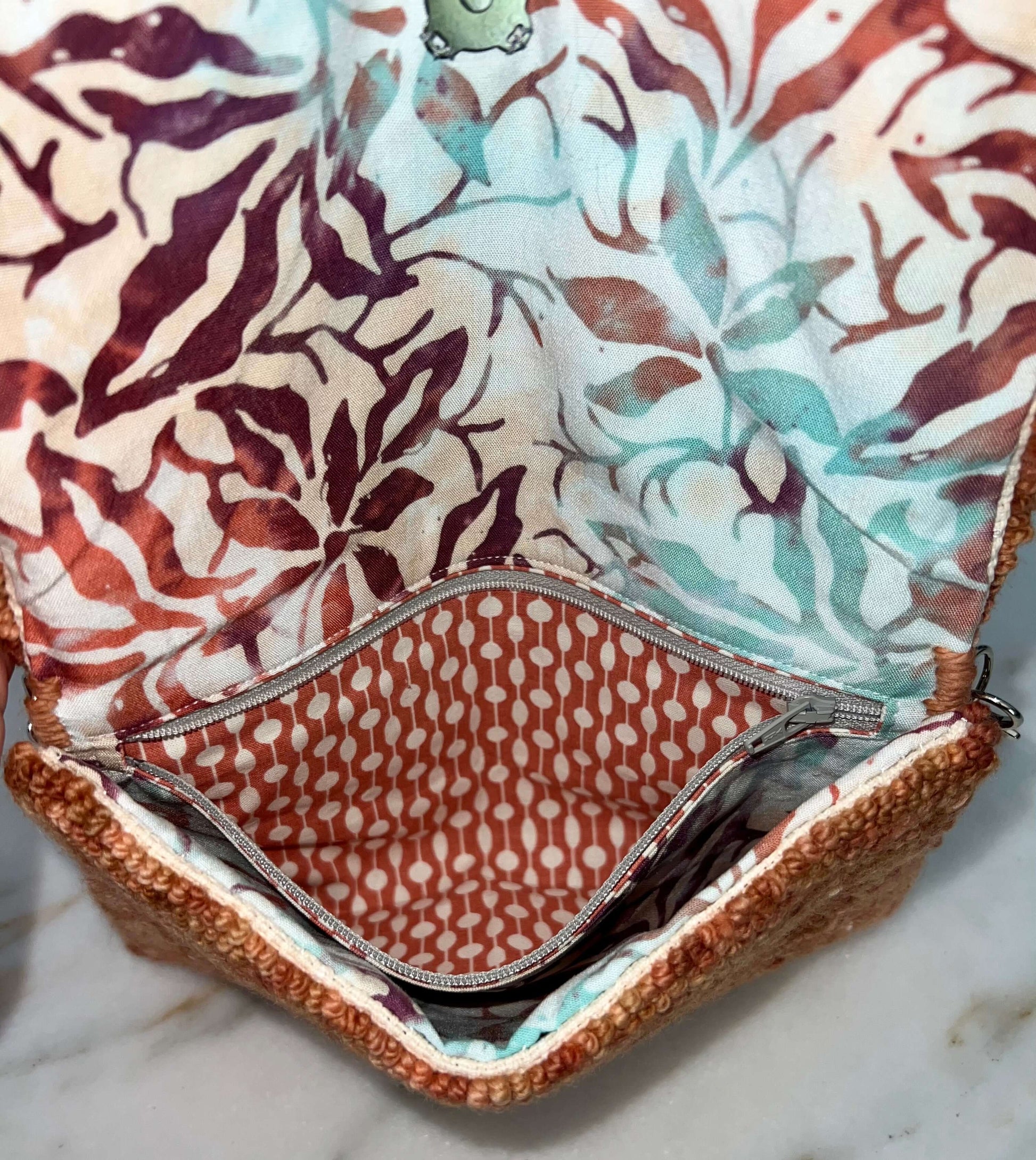 Interior view of a variagated peach clutch bag with floral patterns and a zippered pocket.