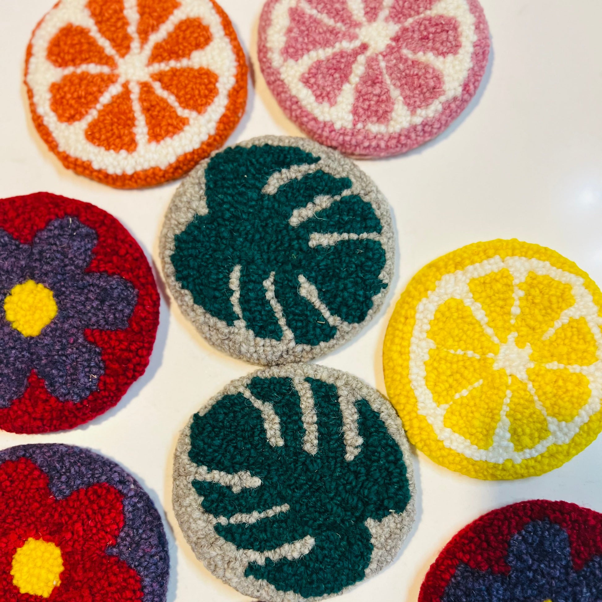 Colorful woven coasters with floral, leaf, and citrus designs on a white background