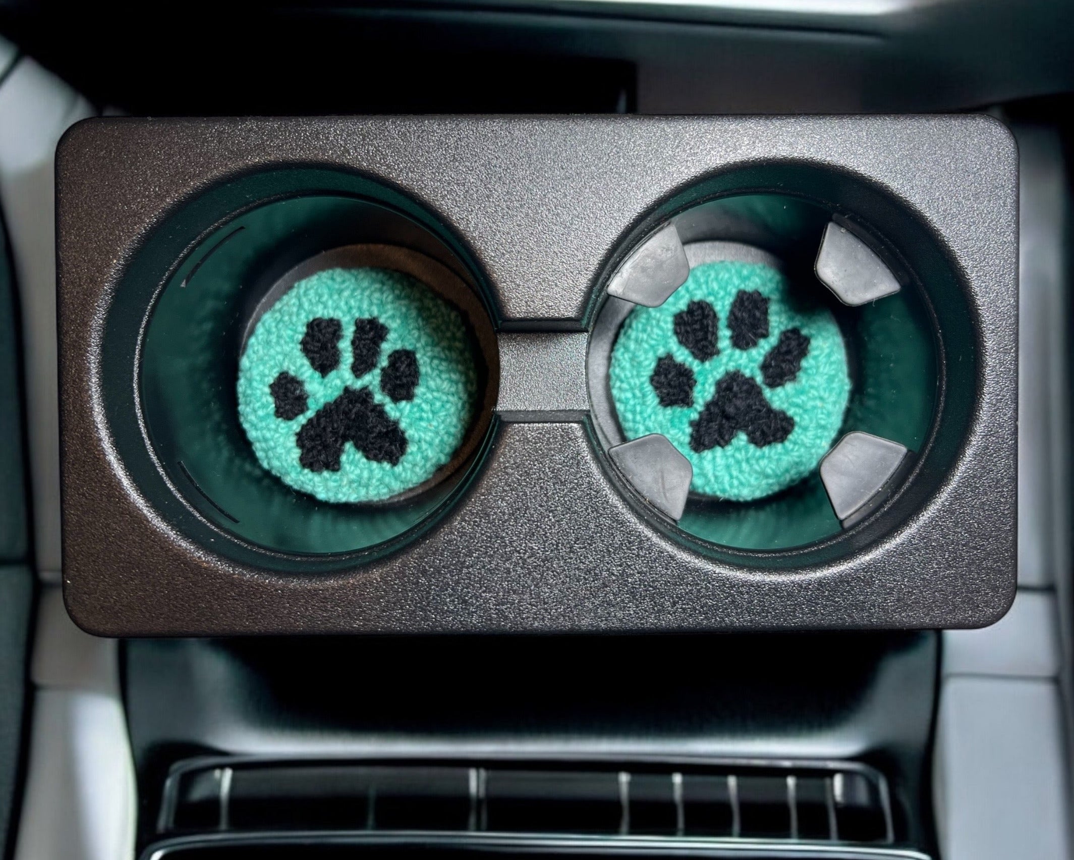 Car cup holder with green paw print coasters inside a vehicle.