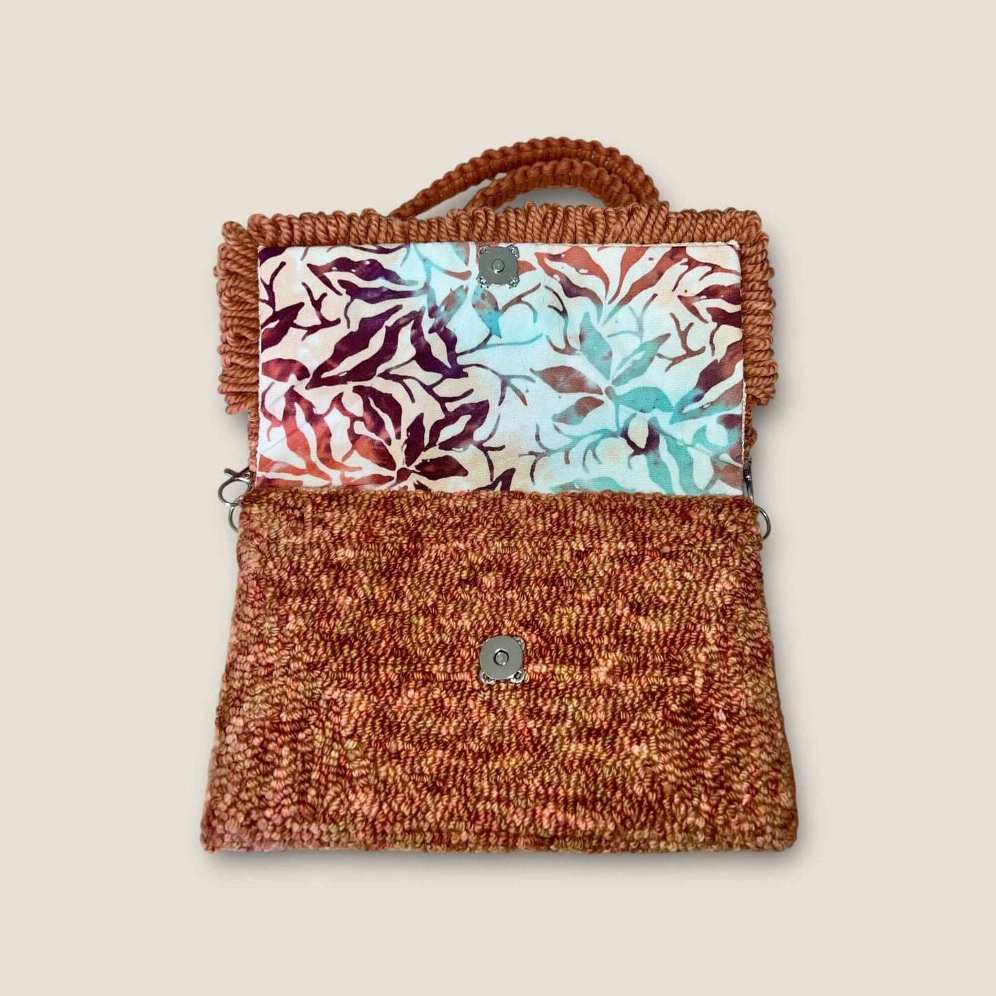 Variagated peach clutch bag with strap featuring vibrant floral design and durable fabric.